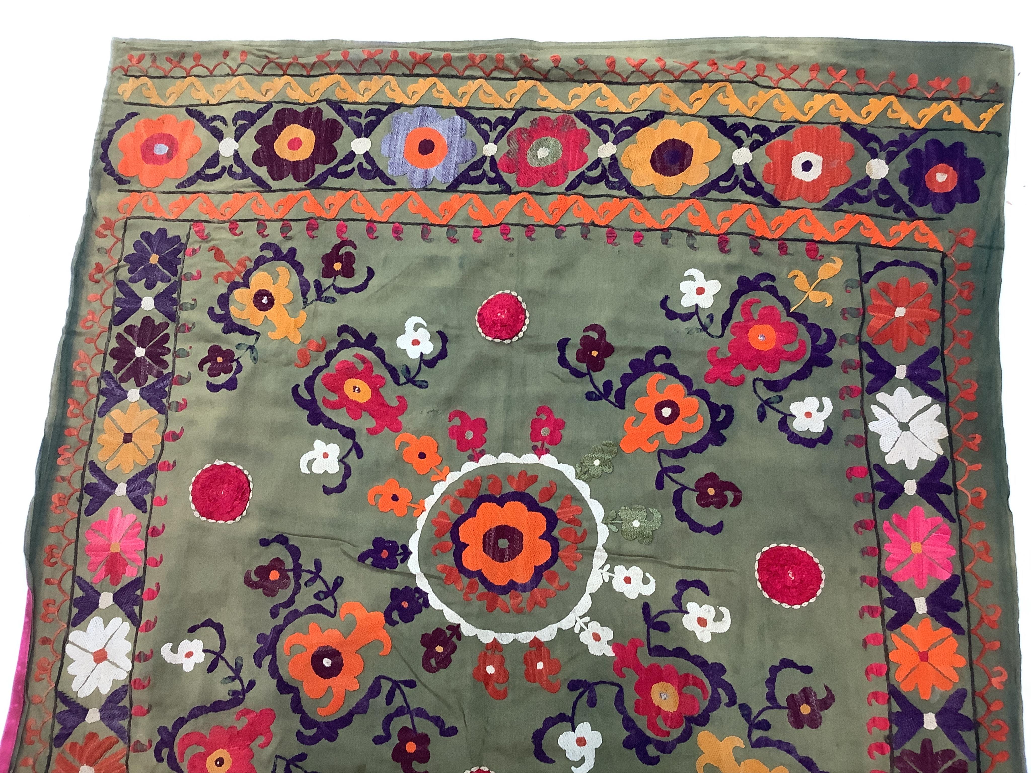 A late 19th early 20th century Suzani table cover. Worked on an olive green cotton in bright polychrome silk threads. Probably from Uzbekistan, made as part of a brides dowry with later lining., 88cm x 98cm. Condition -